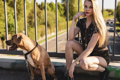 Portrait of young woman with dog sitting by railing on footbridge