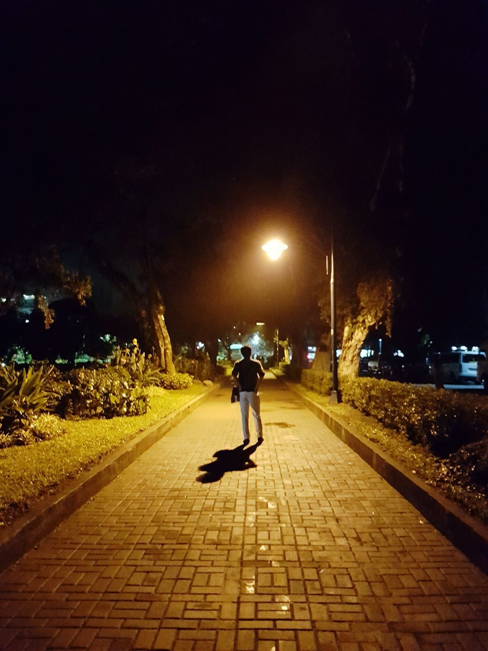 REAR VIEW OF MAN ON ILLUMINATED STREET AGAINST SKY AT NIGHT