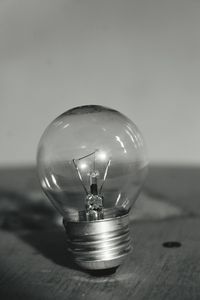 Close-up of light bulb on wooden table against wall