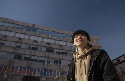 Asian teenage boy with earphones against building on street. madrid. spain