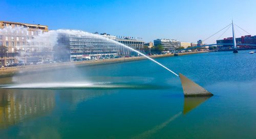 Bridge over river by buildings against clear blue sky