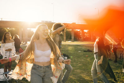 Happy young woman dancing with friends on sunny day in music event