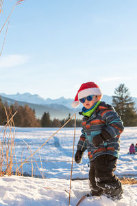 Cute boy wearing warm clothing standing on snow outdoors during winter