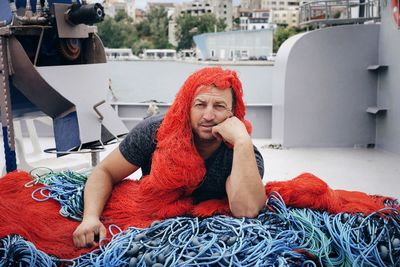 Portrait of man wearing fishing net while sitting at harbor