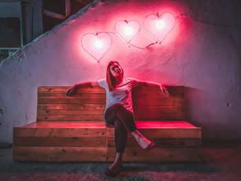 Full length portrait of woman standing against illuminated wall