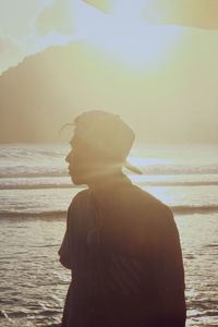 Silhouette teenage boy looking away while standing at beach during sunset