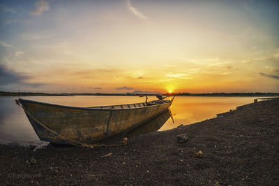 Boat moored on beach against sky during sunset