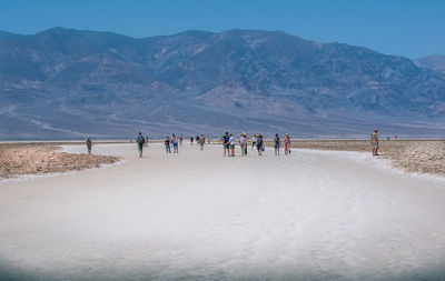 People walking on sand dune by mountain against clear sky