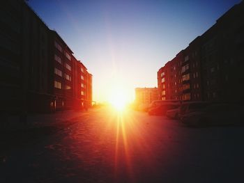 Road amidst buildings against sky during sunset