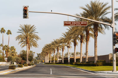 Road sign by palm trees against sky