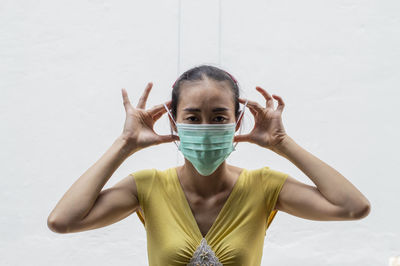 Portrait of woman wearing mask standing against white wall