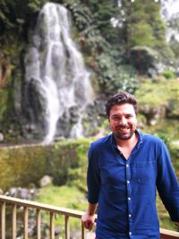 Portrait of man standing by railing against waterfall