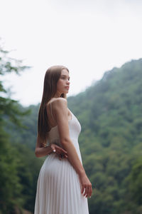 Beautiful young woman standing against by mountain against clear sky