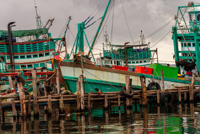 Fishing boats moored at harbor against sky