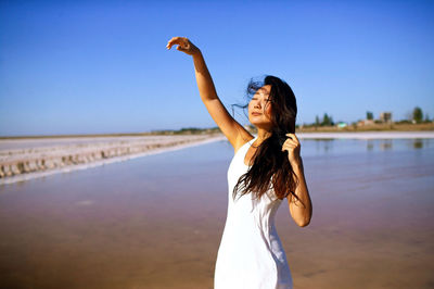 Asian woman in white dress with long dark hair dancing in wind on beach of pink sea.