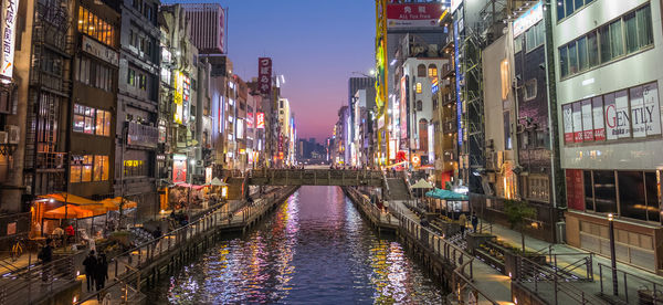 Canal amidst illuminated buildings in city during sunset