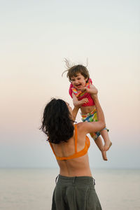 Happy friends standing at beach against clear sky