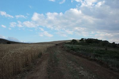 Dirt road amidst field against sky