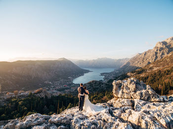 Woman standing on rock by mountain against sky