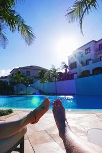 Low section of couple lying on lounge chairs at poolside