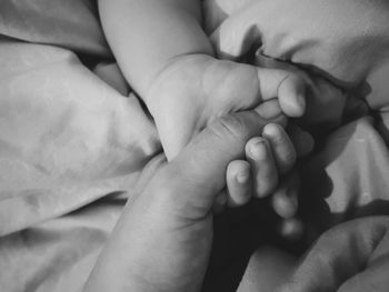 Close-up of baby hands on bed holding mom's hand