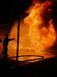 Silhouette of firefighter spraying water on fire at night