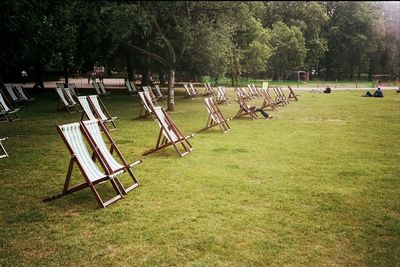 Empty chairs on field against trees