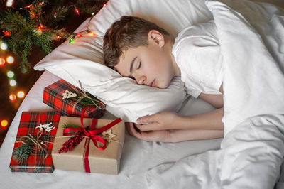 Teenage boy sleeps in bed , with christmas presents lying nearby. christmas morning.