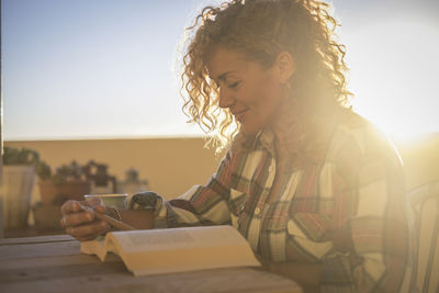 Young woman reading book on table against sky