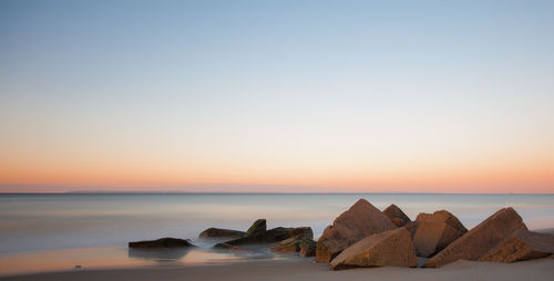 Rocks at beach against clear sky during sunset
