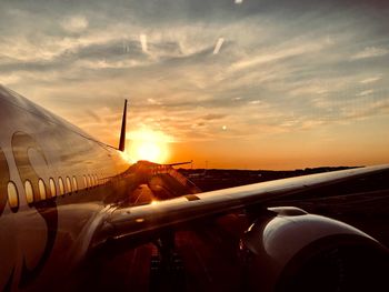 Airplane at airport runway against sky during sunset