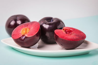 On a white saucer is a large plum, cut in half, and next to it is a whole plum.