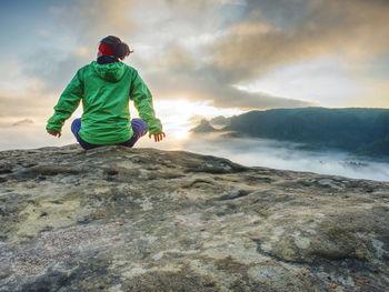 Woman sit on cliff edge and looking to rising sun above misty valley. foggy mountain. man hike