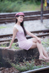 Portrait of woman sitting on railing against railroad tracks