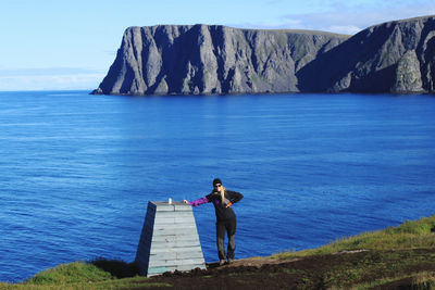 Rear view of woman sitting on rock by sea against sky