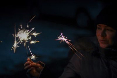 Close-up of woman in fur coat holding lit sparkler at night