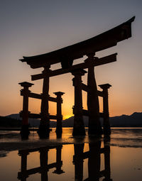 Silhouette cross on lake against sky during sunset