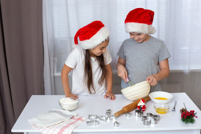 Brother and sister in red caps, stand at a white kitchen table, smile, prepare dough in a bowl