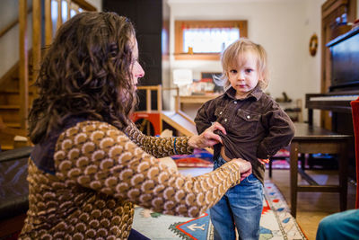 A mother helps her small child get dressed