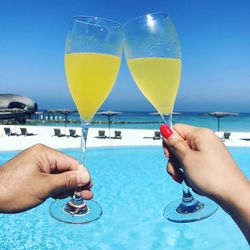 Cropped image of hand holding drink against swimming pool