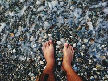 Low section of man standing at sea shore