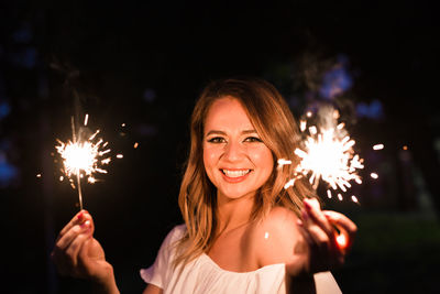 Portrait of smiling woman with fire crackers at night