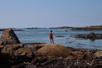 Rear view of person standing on rock by lake against sky