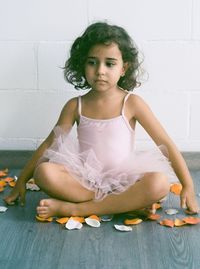 Sad girl in ballet dress sitting legged crossed against wall at home