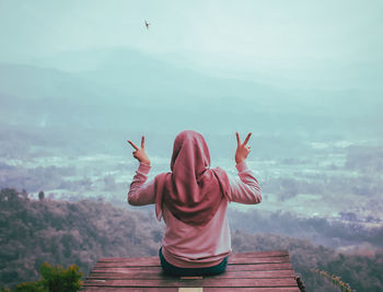 Rear view of woman with arms raised on mountain against sky