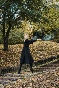 Ballerina dancing in autumn city street, modern ballet dancer in black dress, pointe shoes outdoors