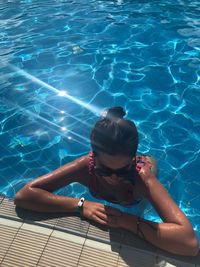 High angle view of young woman wearing sunglasses swimming in pool during sunny day