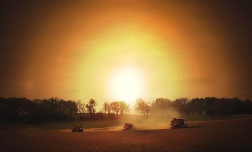 Cars on field against sky during sunset