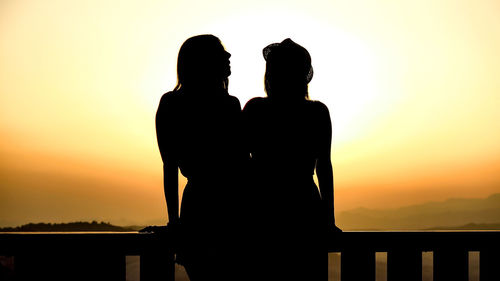 Silhouette couple standing against orange sky