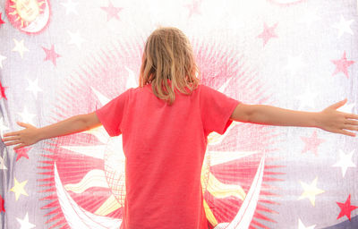 Rear view of woman with arms raised standing against pink wall